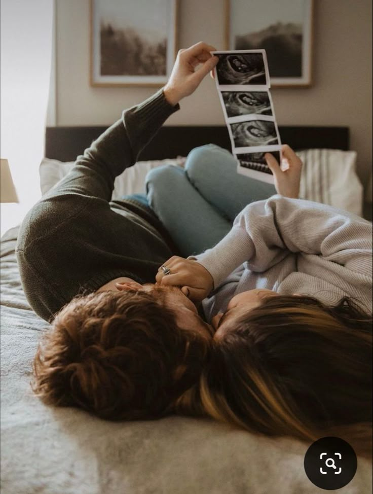 a woman laying on top of a bed holding up a photo