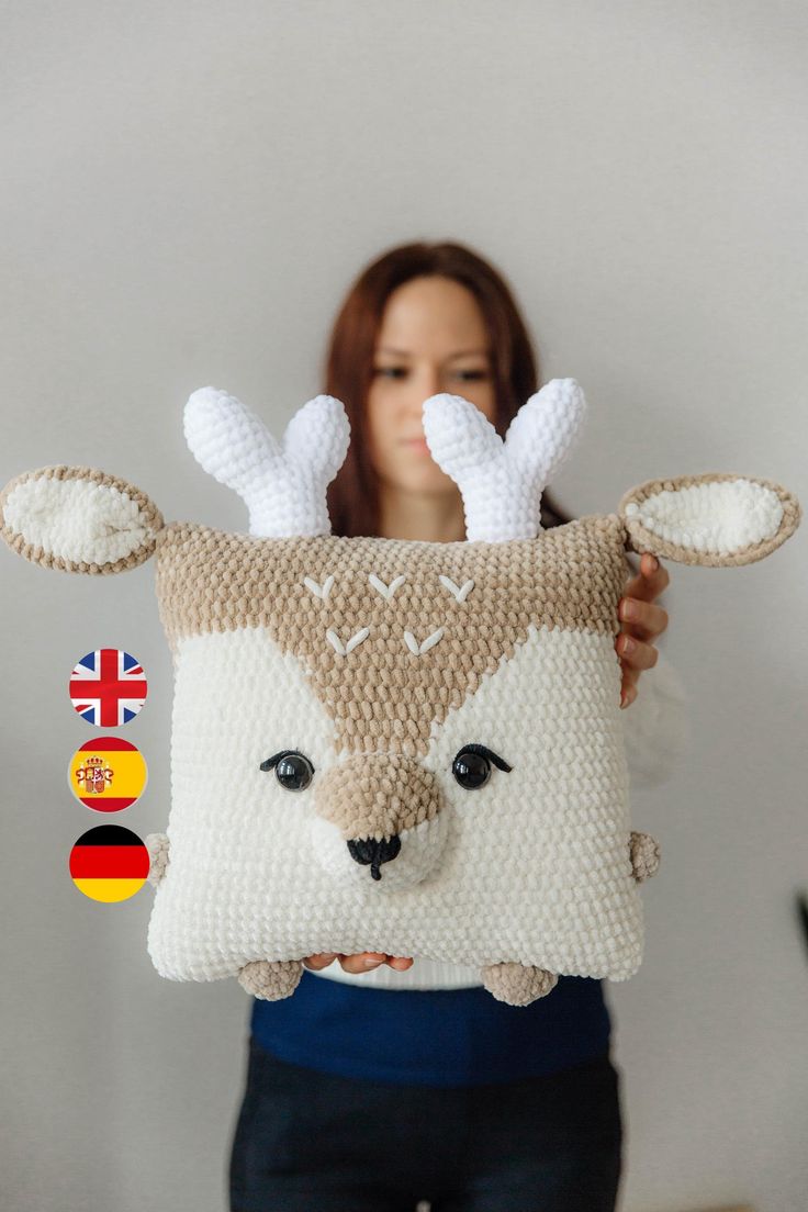 a woman holding up a knitted pillow with deer's head on the front