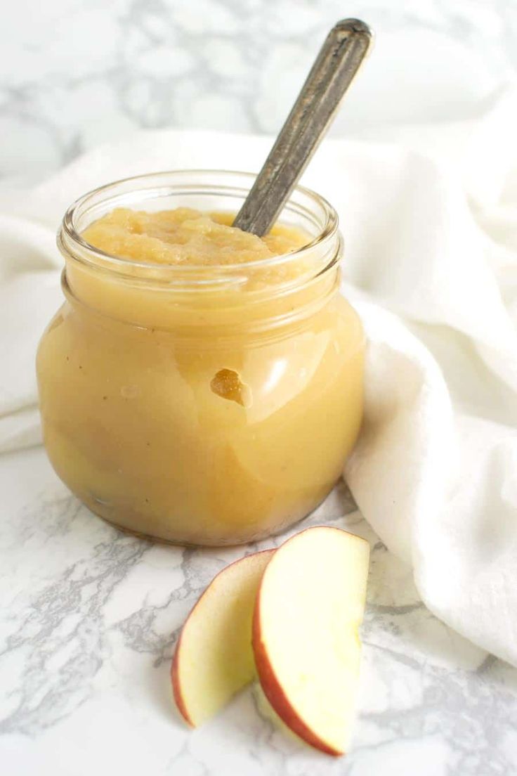 an apple pie in a glass jar with a spoon next to it on a marble surface