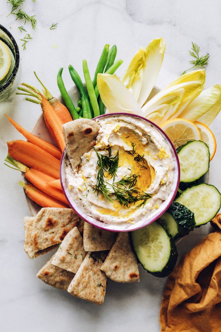 hummus, carrots, celery, cucumbers and crackers on a plate