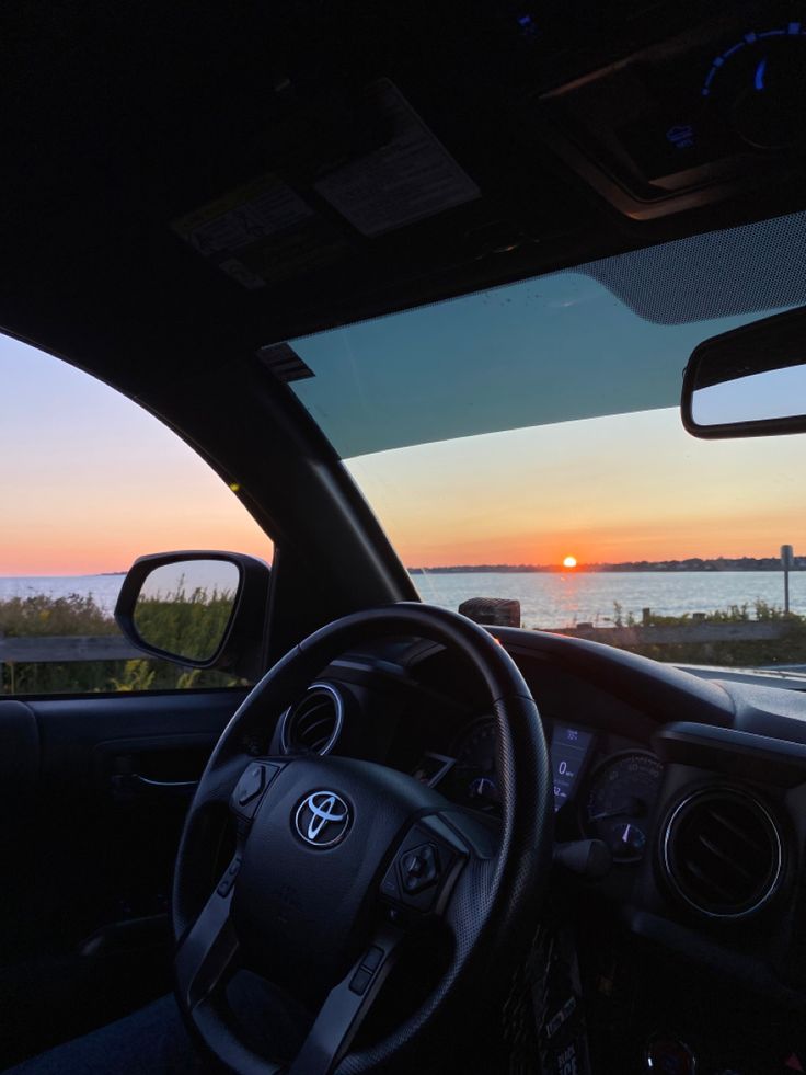 the sun is setting in the distance as seen from inside a car with dashboard and steering wheel