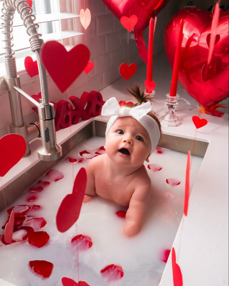 a baby laying in a bathtub surrounded by red hearts and streamers on the floor