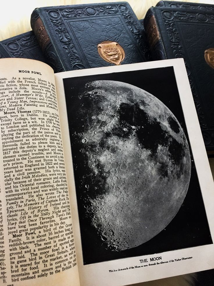 an open book sitting on top of a table next to two books with pictures of the moon