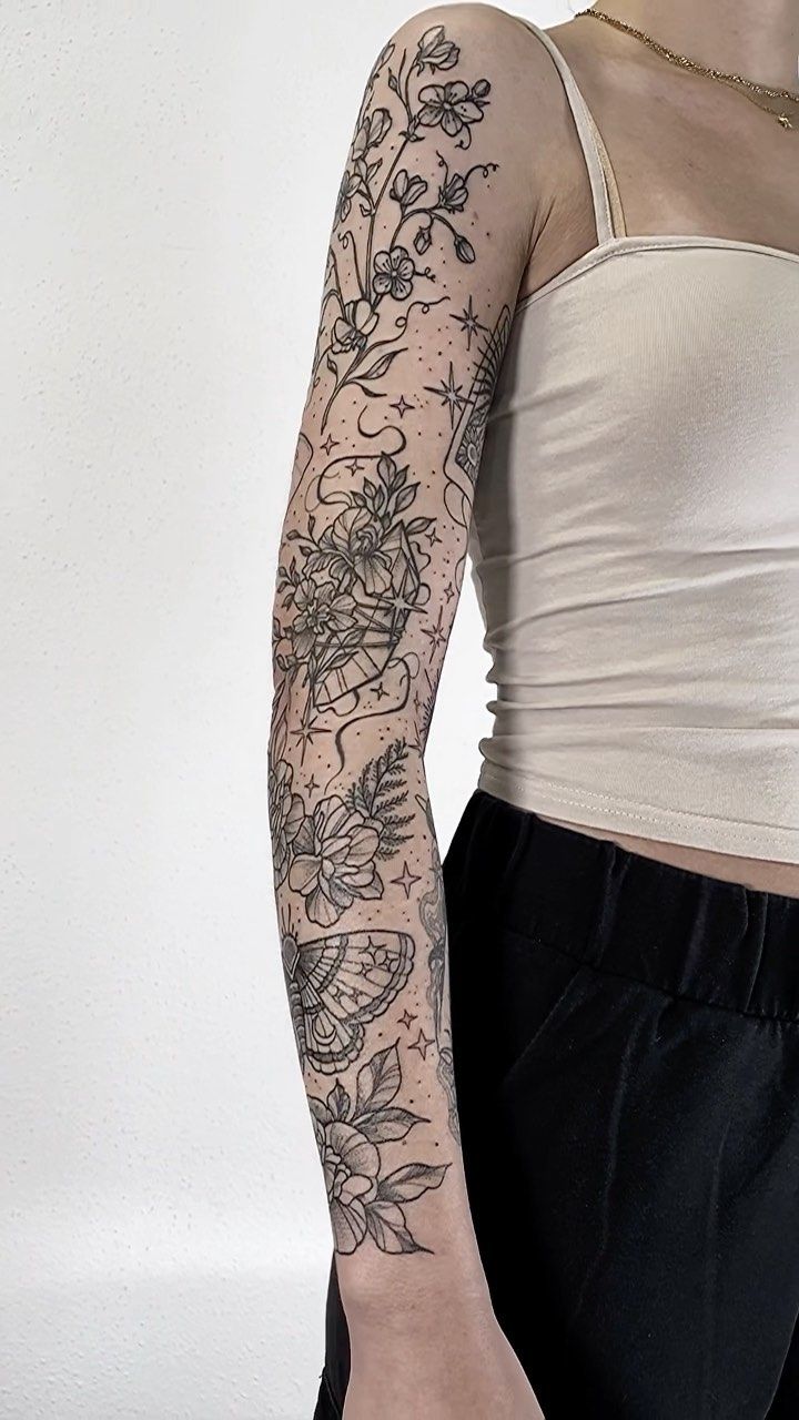 a woman with a flower tattoo on her arm and shoulder, standing in front of a white wall