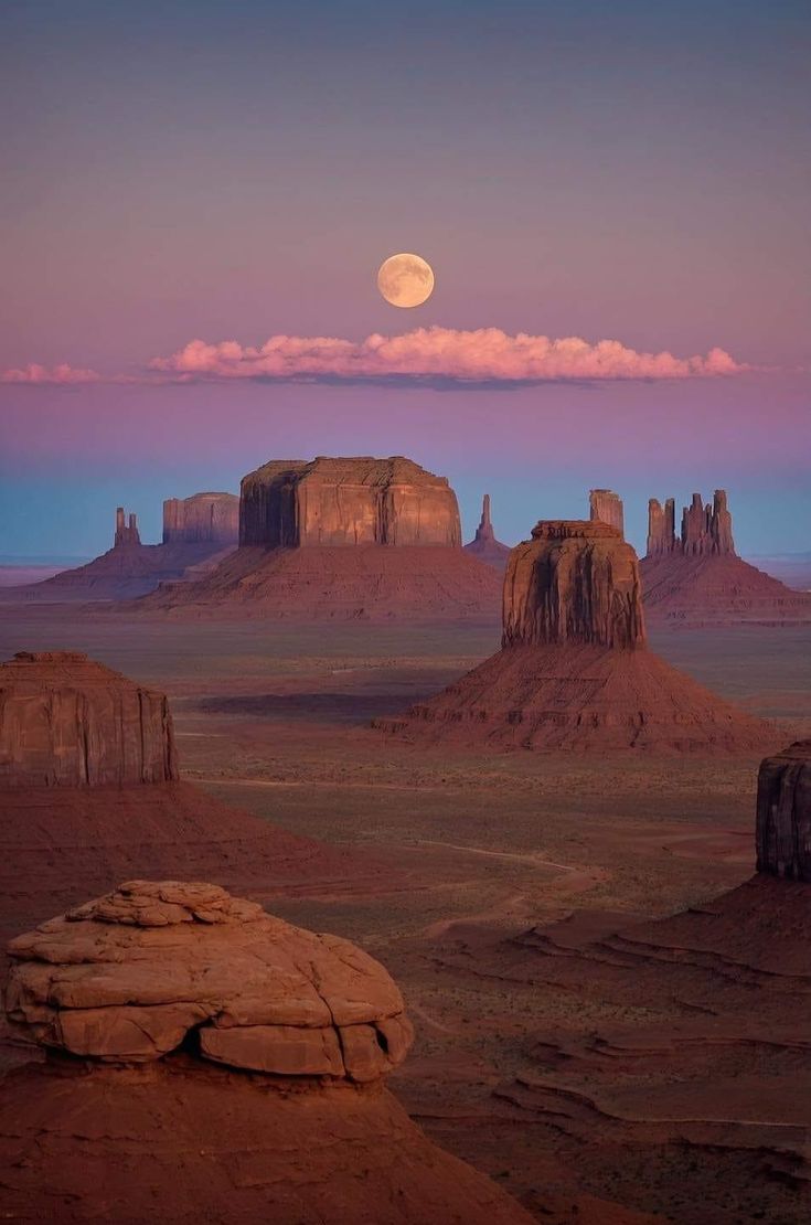 the moon is setting over monument formations in the desert