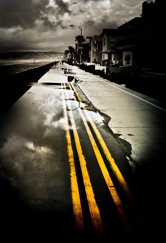 an empty street with yellow lines painted on the side and dark clouds in the background