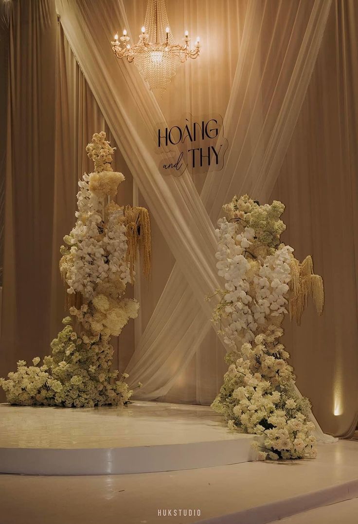 two tall vases filled with flowers sitting on top of a white tablecloth covered stage