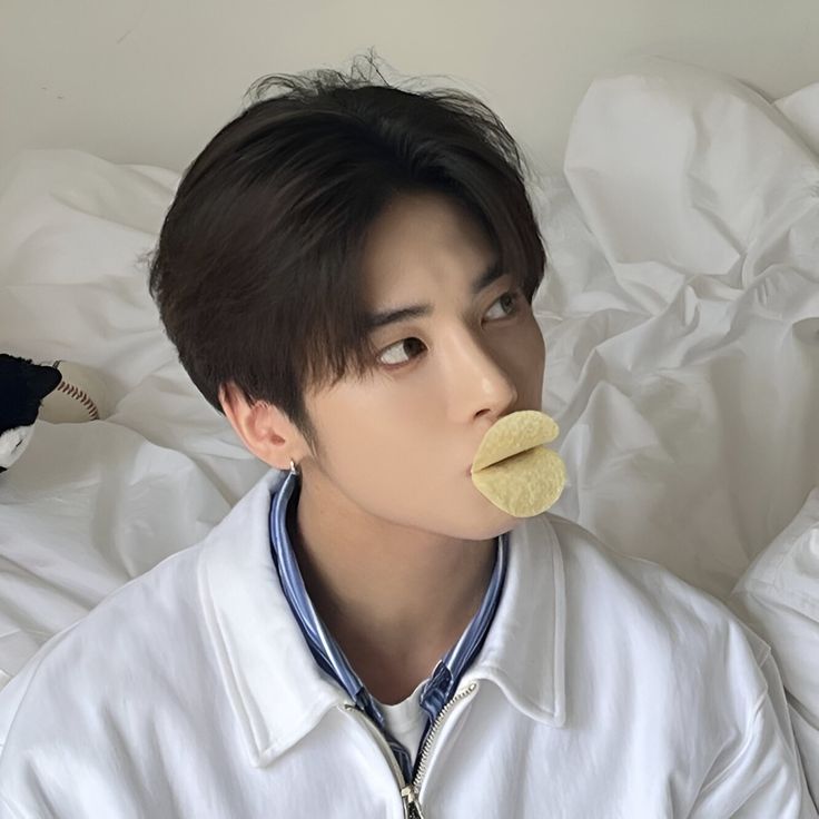 a man laying on top of a bed with a banana in his mouth while wearing a white shirt