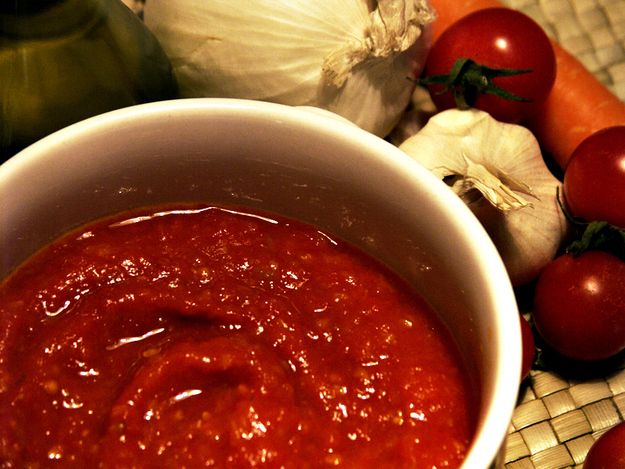 a white bowl filled with sauce next to garlic and tomatoes