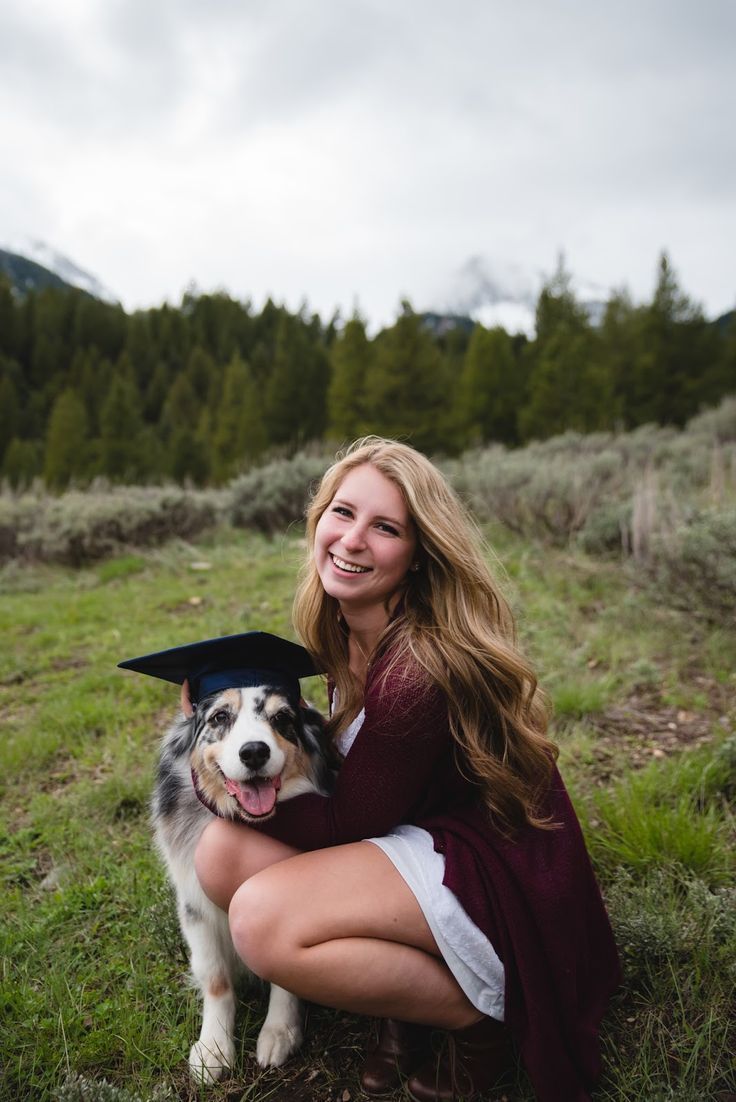 a woman is sitting in the grass with her dog wearing a graduation cap and gown