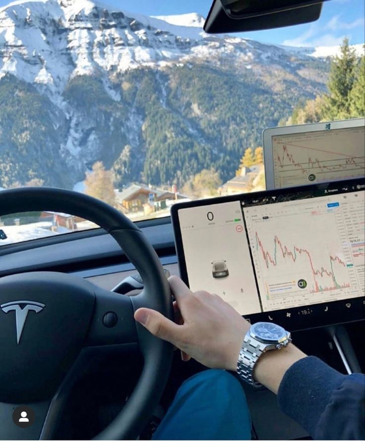 a person driving a car with a laptop on their lap and mountains in the background