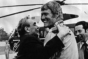 two men are hugging each other in front of a helicopter while another man holds his arm around him