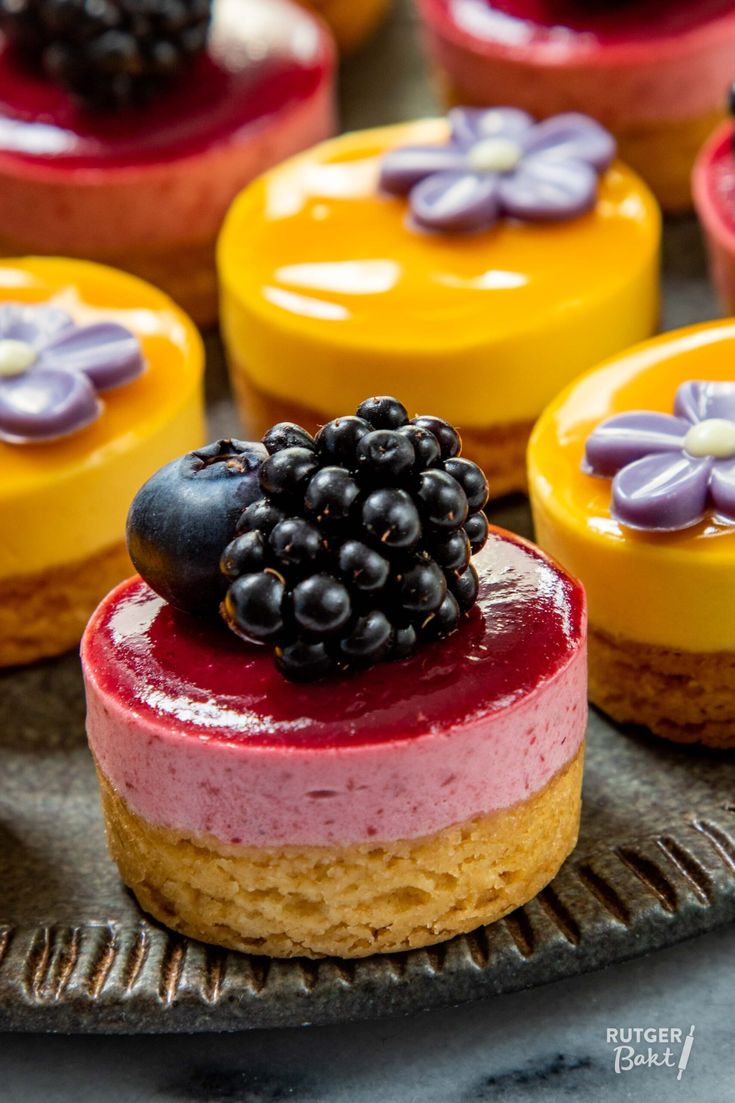 several desserts are arranged on a plate with purple and yellow frosted toppings