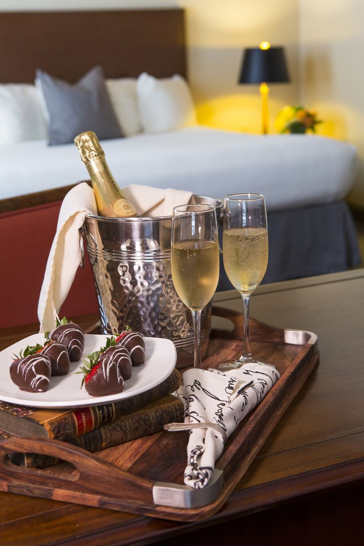 champagne and chocolate covered strawberries on a tray in front of a king size bed