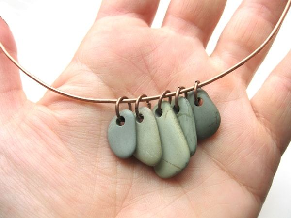 a hand holding a wire wrapped necklace with four different colors of clay beads hanging from it