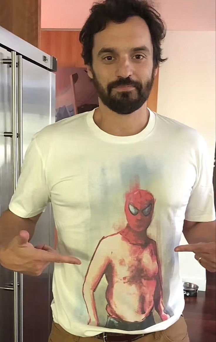 a man with a beard wearing a spiderman t - shirt in front of a refrigerator