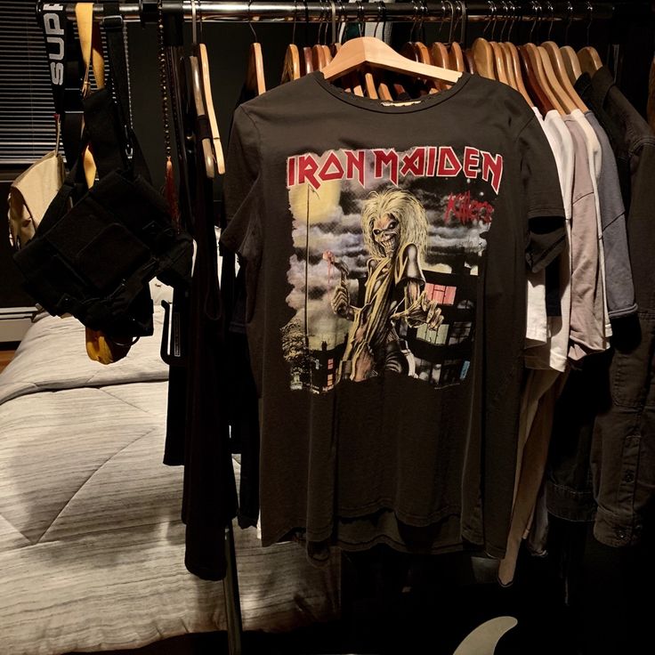 an iron maiden shirt hanging on a rack in a closet with clothes and other items