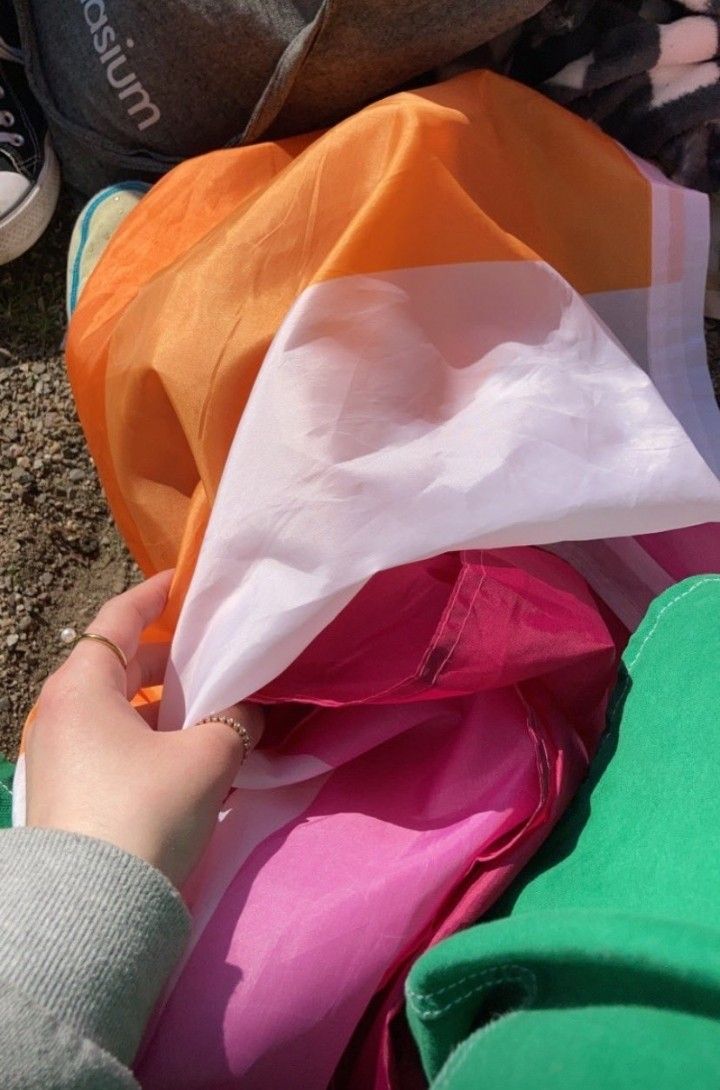 a person is holding an orange, white and pink kite while another person sits on the ground