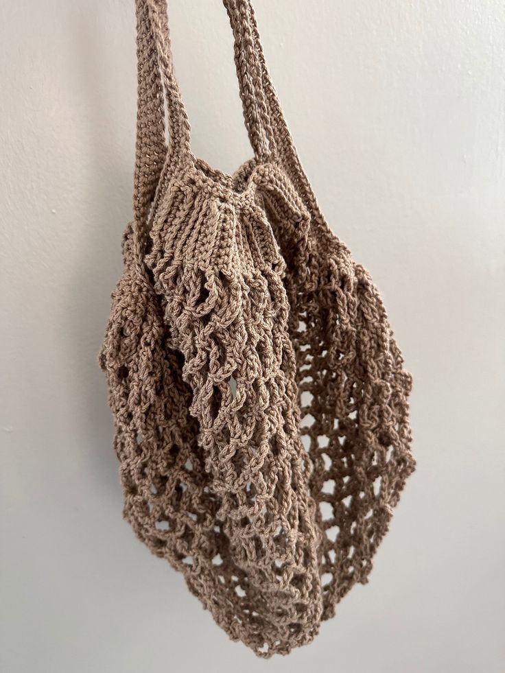 a crocheted bag hanging from a hook on a wall with white walls in the background