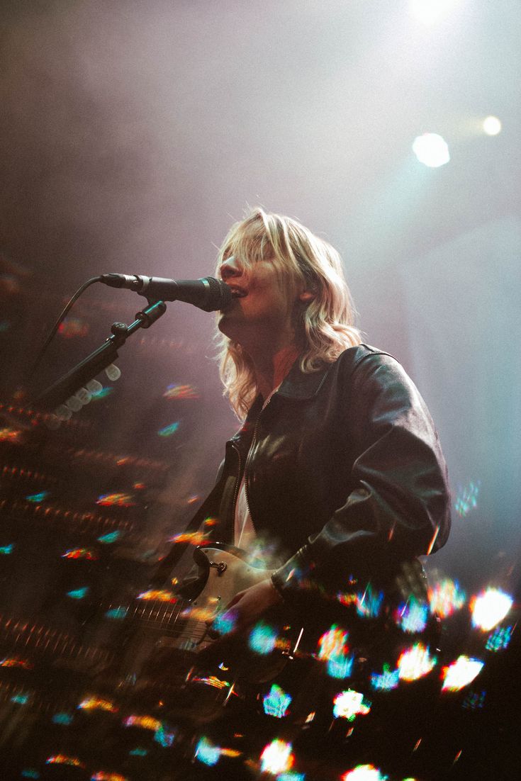 a man that is standing up with a guitar in front of some microphones and lights