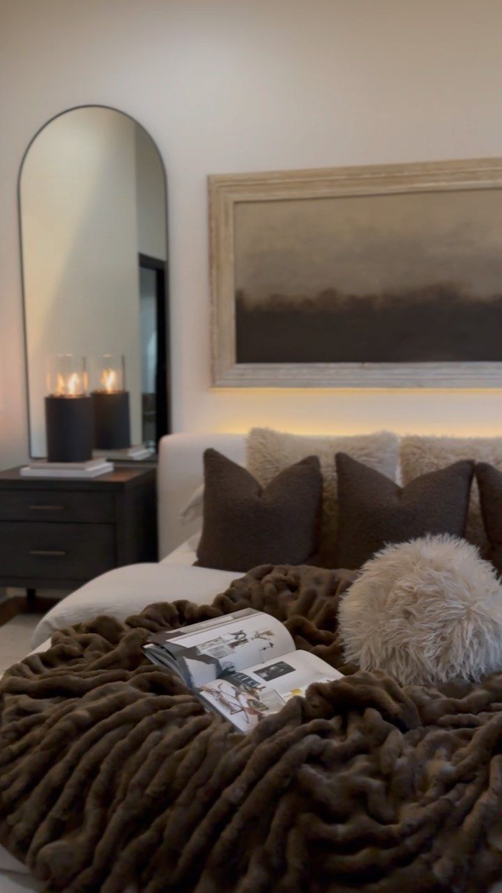 a bed with pillows and blankets on top of it in a bedroom next to a mirror