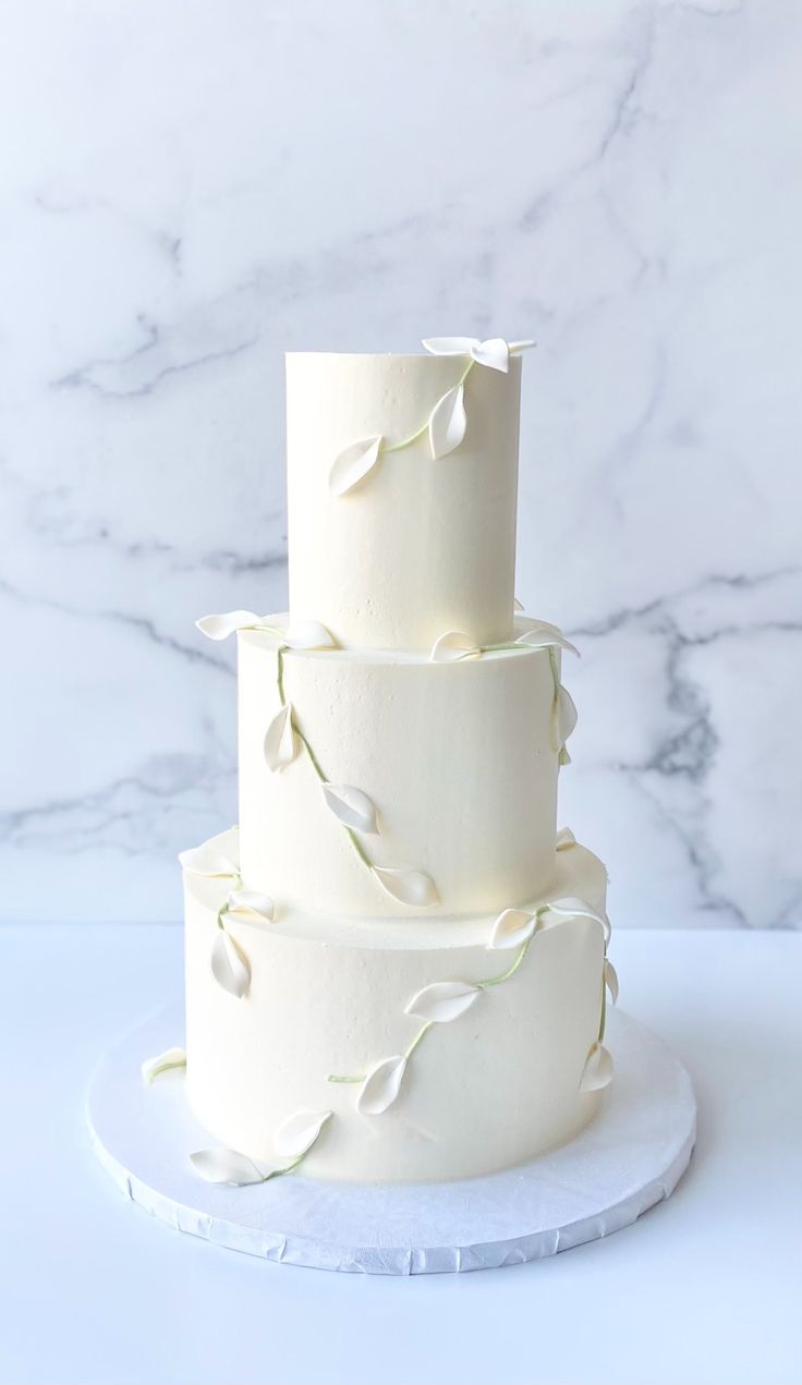 a three tiered white wedding cake with flowers on the top and bottom, sitting on a marble platter