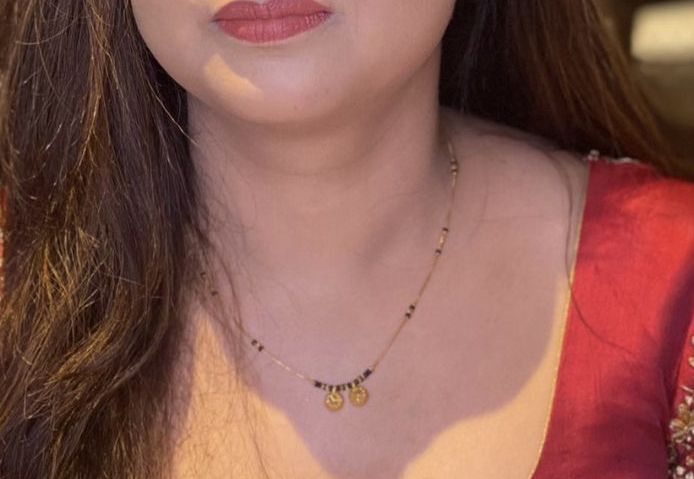 a close up of a woman wearing a red shirt and gold necklace on her neck