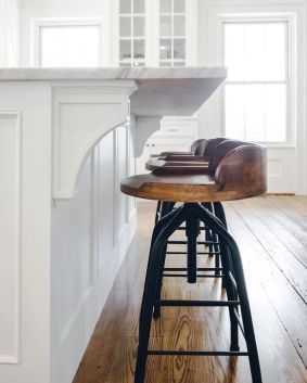 a kitchen with white walls and wood floors, an island countertop and bar stools