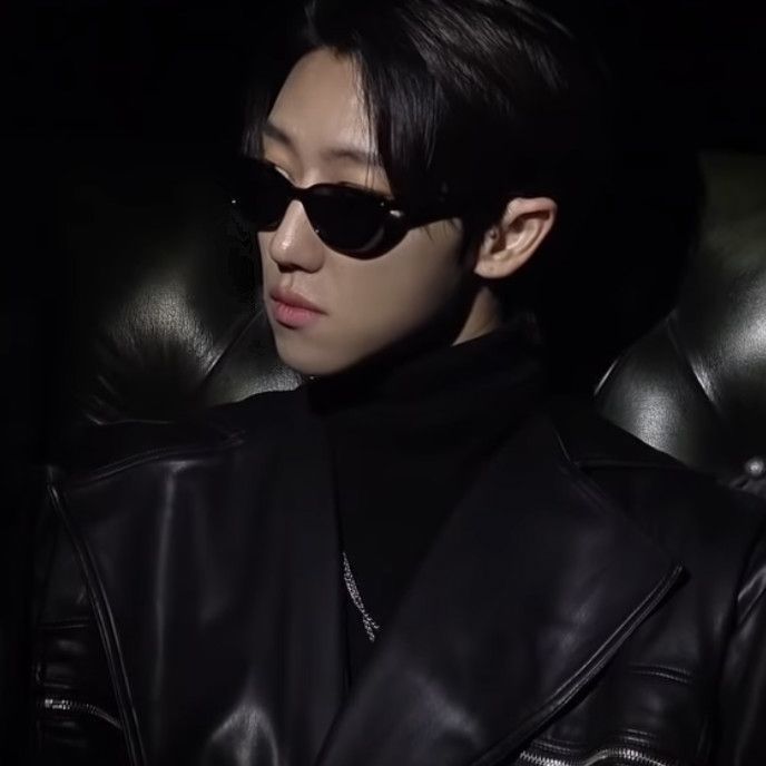 a young man wearing sunglasses sitting in a black leather chair and looking off to the side