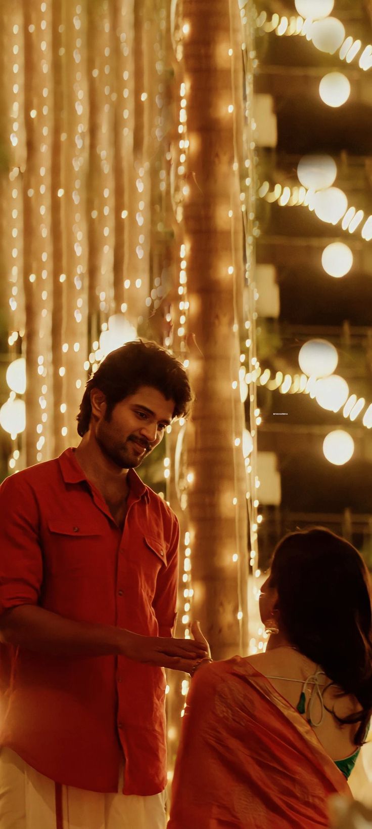 a man and woman standing next to each other in front of some stringed lights