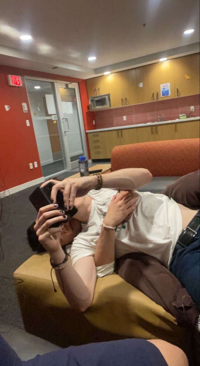 two people are laying on a couch and one is holding a cell phone while the other person takes a selfie