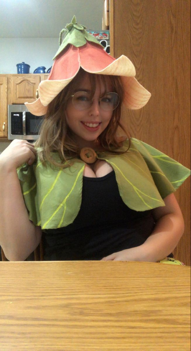 a woman wearing a hat with leaves on it sitting at a table in the kitchen