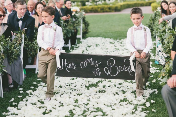 two young boys standing in front of a sign that says here comes the bride