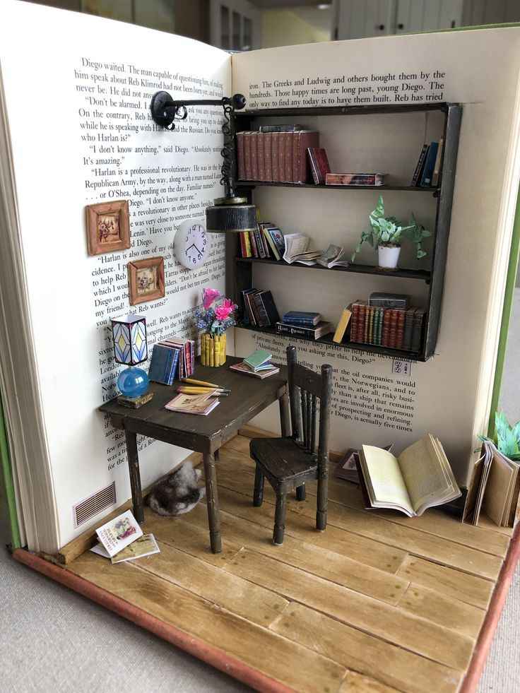 an open book with a miniature table and chair in front of it on top of a wooden floor