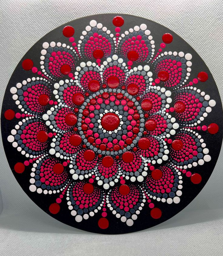 a red and white flower painted on a black circle with circles in the shape of dots