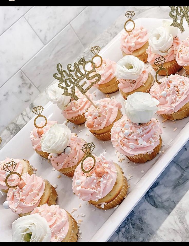 cupcakes with pink frosting and gold numbers on them are arranged in a white tray