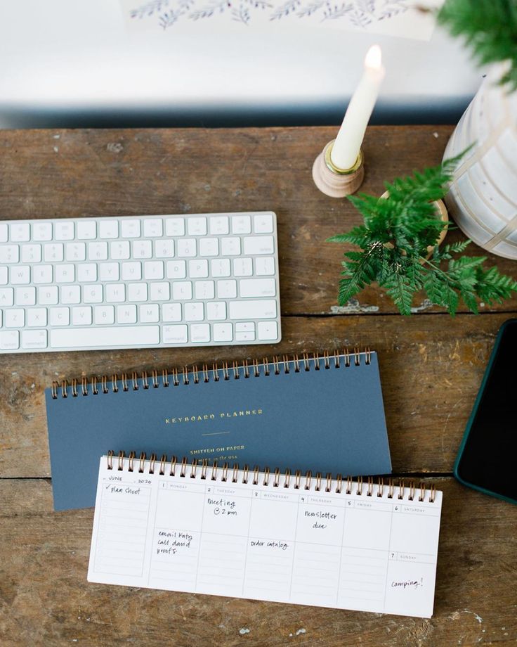 a desk with a calendar, keyboard and plant on it next to a phone in front of a computer