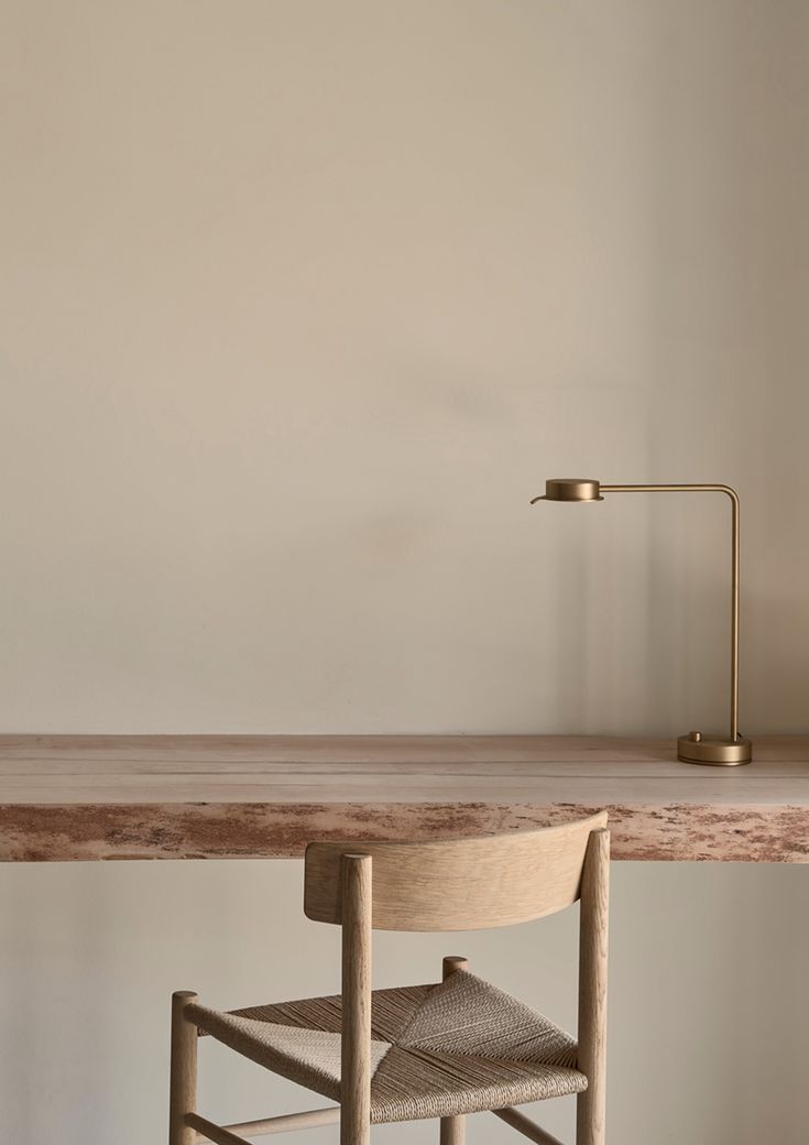 a wooden table with a chair and lamp on top of it in front of a white wall