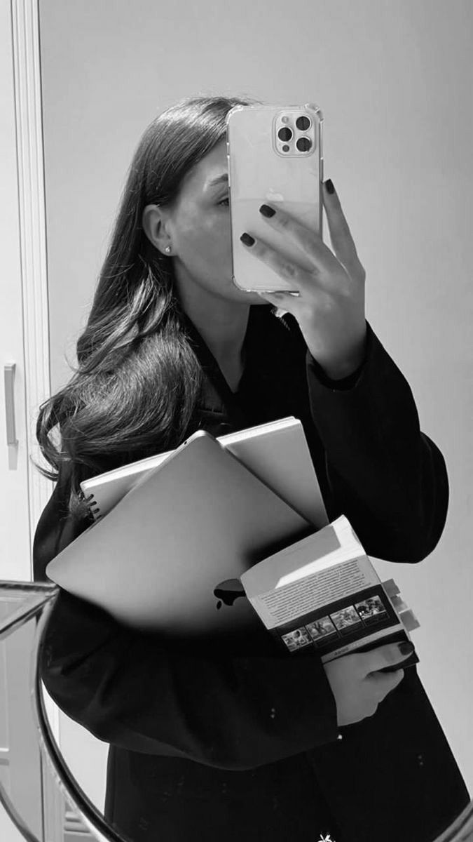 a woman taking a selfie in front of a mirror with her cell phone and books