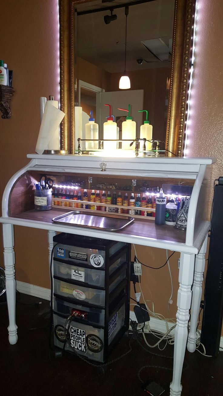 a white desk with drawers under a mirror and lights on it's sides, in front of a pink wall