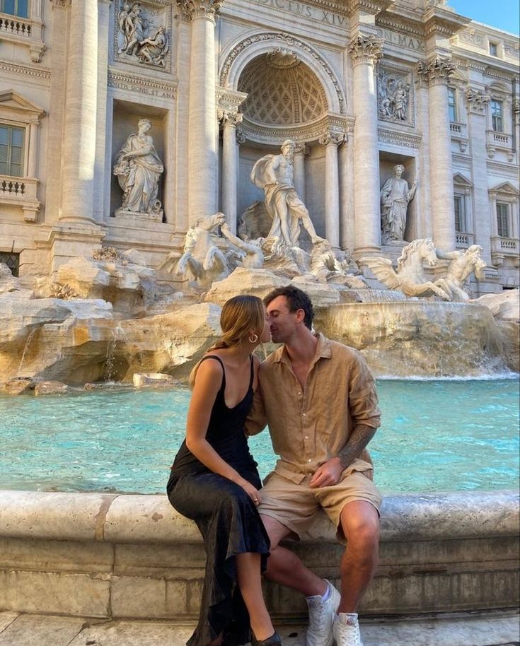 a man and woman sitting on the edge of a fountain in front of a building