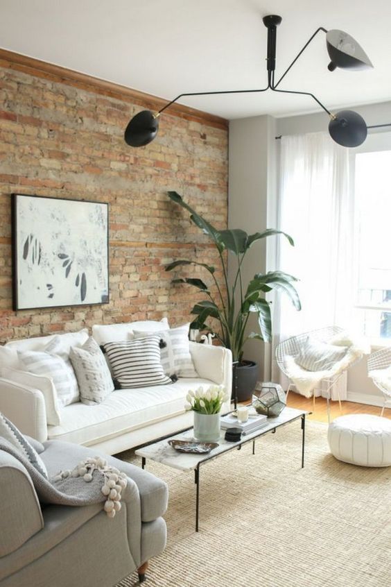 a living room filled with furniture and a brick wall behind the couch is a large potted plant