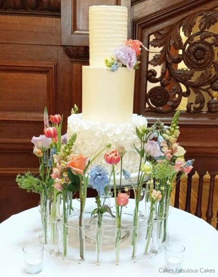 a wedding cake with flowers on the top is sitting on a table in front of some wine glasses