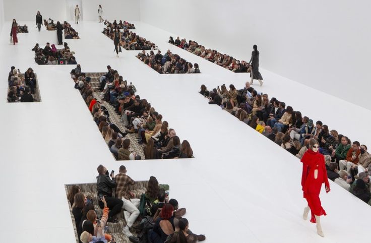 a model walks down the catwalk in front of a large group of seated people