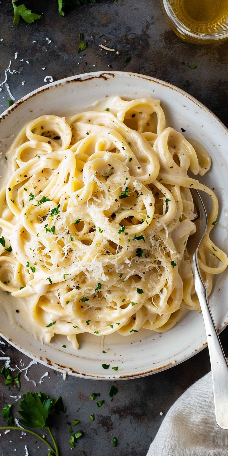 a white bowl filled with pasta and parsley on top of a gray table next to a glass of beer