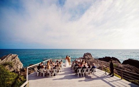 a group of people standing on top of a wooden walkway next to the ocean with chairs