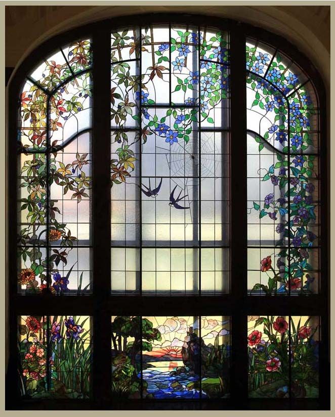 an arched window with stained glass and flowers on the outside, in front of a stone wall