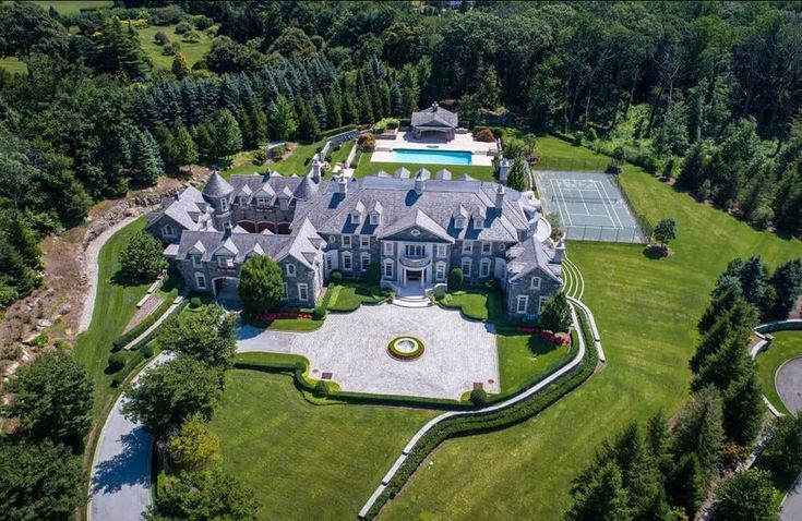 an aerial view of a large mansion in the middle of a wooded area with tennis courts