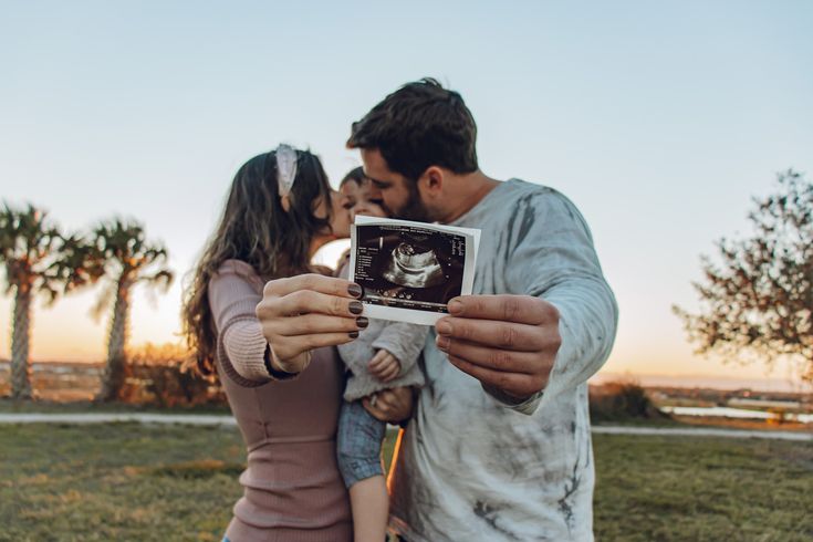 a man and woman taking a photo with a baby in front of palm trees at sunset