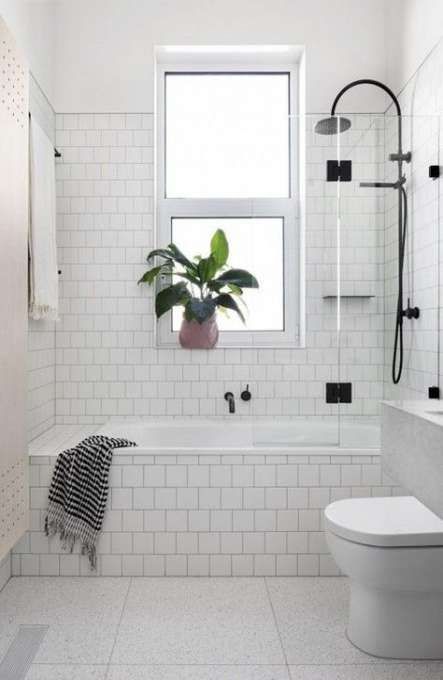 a white tiled bathroom with a toilet, bathtub and window in the corner that has a potted plant next to it